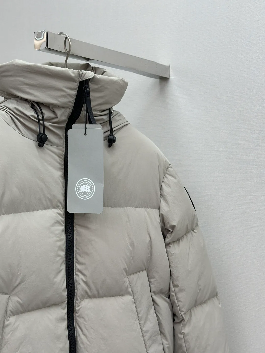 P1010 Canada Goose Black Label Badge Hooded Down Jacket (khaki) The high-quality filling is made of 90 national standard high-quality white duck down, selected high-loft velvet, weighing 240g, light and warm, with excellent temperature locking performance and good resilience. The fabric is woven with 400T high-count yarn. After special water-repellent treatment, the surface forms a lotus leaf effect - raindrops will slide down like beads, and snow particles will fall off when touched. The tear resistance reaches 200N (approximately 20kg load-bearing), the light gray matte texture breaks the stereotype of "outdoor clothing = hardcore", and the soft luster presents a high-end matte effect under urban neon lights, seamlessly switching scenes from ski resorts to CBD office buildings. The ribbon is woven with polyester as the base, and the brand letters are decorated on the ribbon through high-precision computer embroidery. The edges of the pattern are clear, the stitches are fine and even, and multiple layers of embroidery thread are stacked to enhance the three-dimensional effect. Precision thread reinforcement prevents linting and ensures the fluffy and resilient elasticity lasts as new. The embedded cuffs are three-dimensionally woven to form a "wavy" elastic structure, which forms natural folds when fitting the wrist, increasing the contact area with the skin, thus improving the windproof effect. At the same time, micro-velvet treatment is added to the inside of the cuffs, which feels like a second layer of skin and avoids friction on the skin from metal zippers or hard fabrics. Size:S-M-L-XL